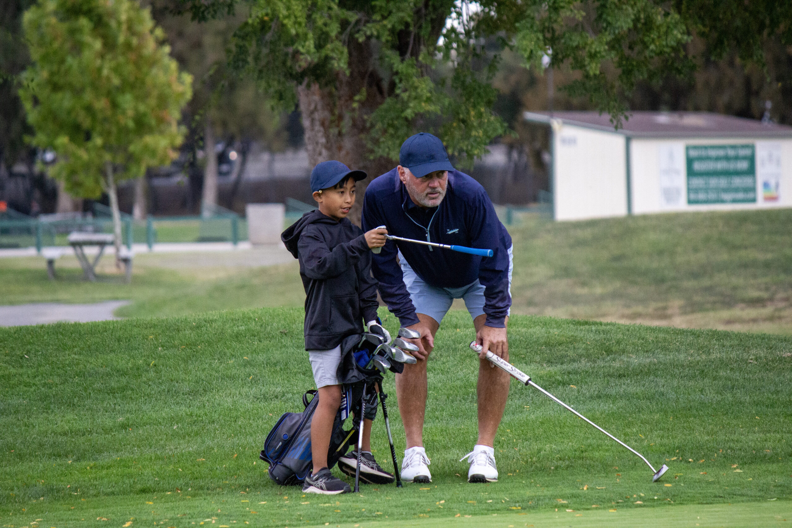 A golf mentor and a young golfer on the field together looking down the green.